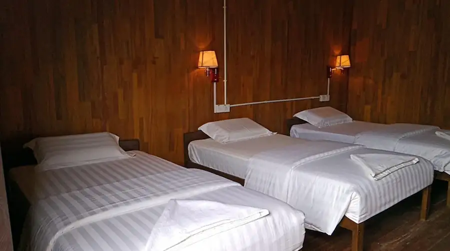 Cozy rustic room interior at Kulapuan Resort featuring wood-paneled walls and three comfortable single beds for group stays.