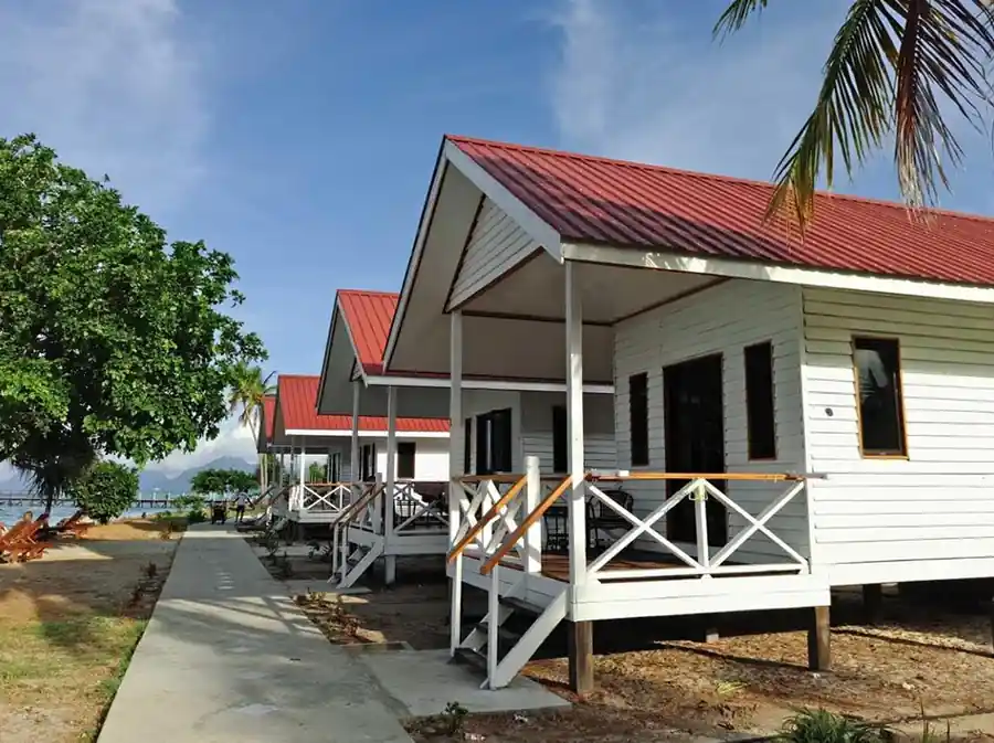 Exterior view of the beautiful white wooden beach chalets with red roofs along a paved pathway at Kulapuan Resort in Semporna.